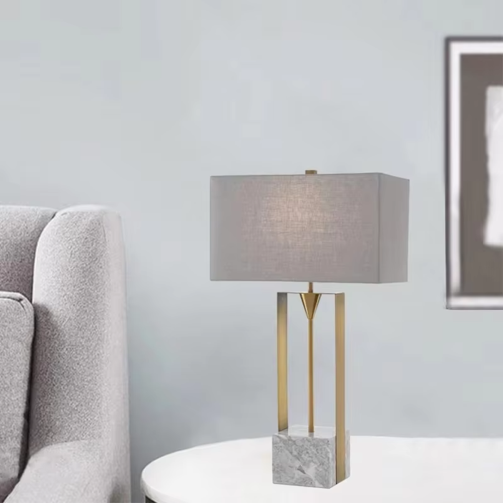 This is a modern minimalist table lamp with a golden metal frame, a marble base, and a gray fabric square lampshade, featuring a simple and elegant design. It is used for local desktop lighting and decoration, combining practicality and aesthetics. It is suitable for modern home living room side tables, bedroom bedside tables, high-end hotel guest rooms, luxury office spaces and other places.