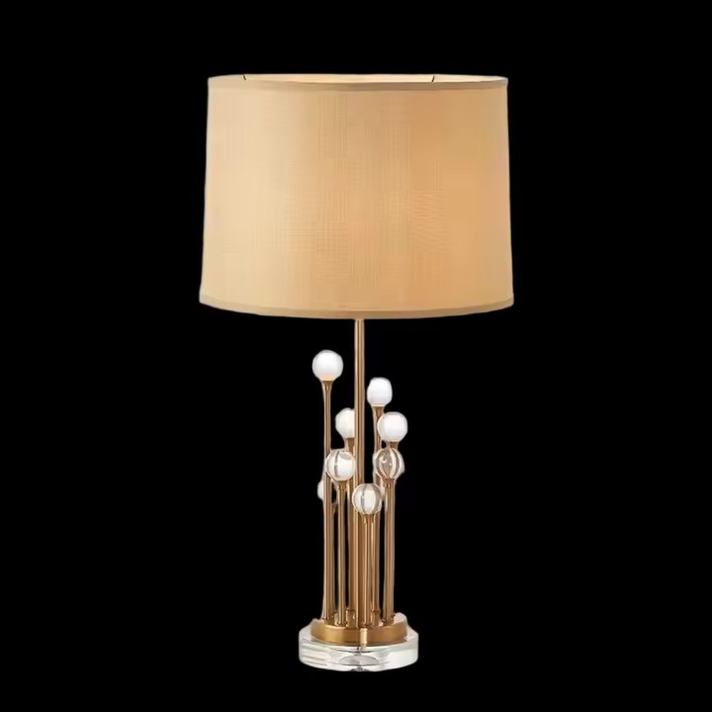 This is a modern luxury-style table lamp with a golden metal stand, multiple spherical decorations, and a beige fabric lampshade that transmits light softly. It has an exquisite and layered design. It is used for local desktop lighting and decoration, combining practicality and aesthetics. It is suitable for modern home living room side tables, bedroom bedside tables, as well as high-end hotel guest rooms, luxury cafes and other places.