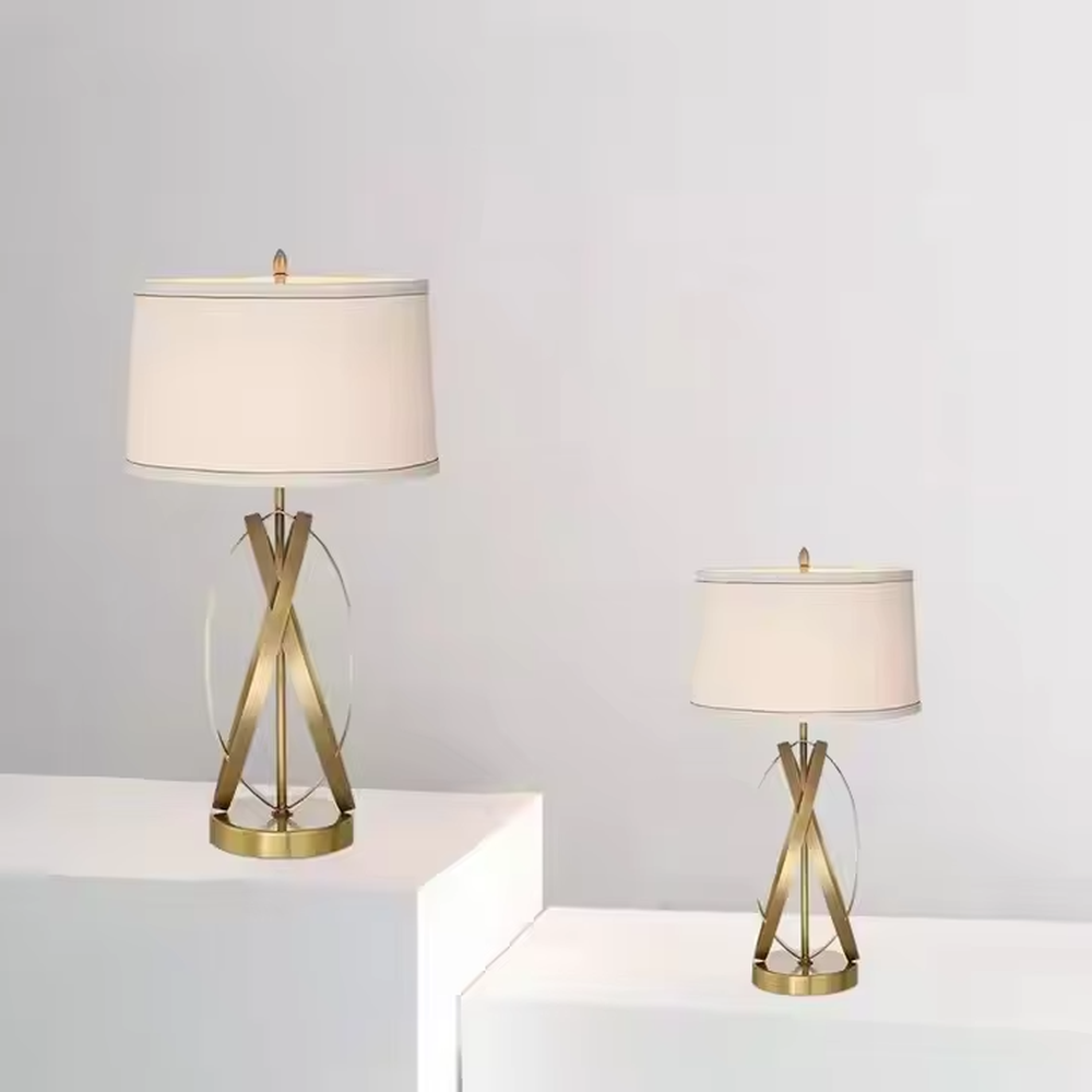 This is a luxury-style table lamp with golden crossed metal brackets and a beige fabric lampshade. It features a simple and elegant design with excellent texture. It is used for local desktop lighting and decoration, creating a luxurious and warm ambiance. It is suitable for luxury-style home bedroom bedside tables, high-end hotel guest rooms, modern office spaces and other places.
