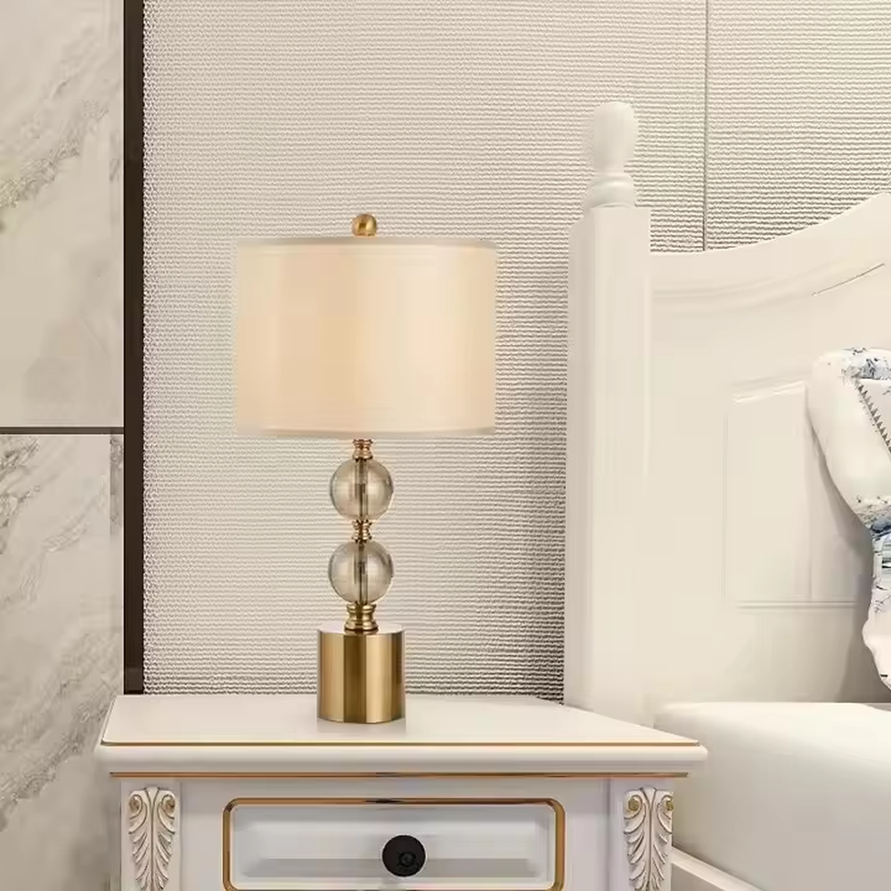 This is a luxury-style table lamp with a golden base, transparent glass spherical body, and beige fabric lampshade. It features a simple and elegant design with excellent texture. It is used for local desktop lighting and decoration, creating a luxurious and warm ambiance. It is suitable for luxury-style home bedroom bedside tables, high-end hotel guest rooms, modern apartment living spaces and other places.