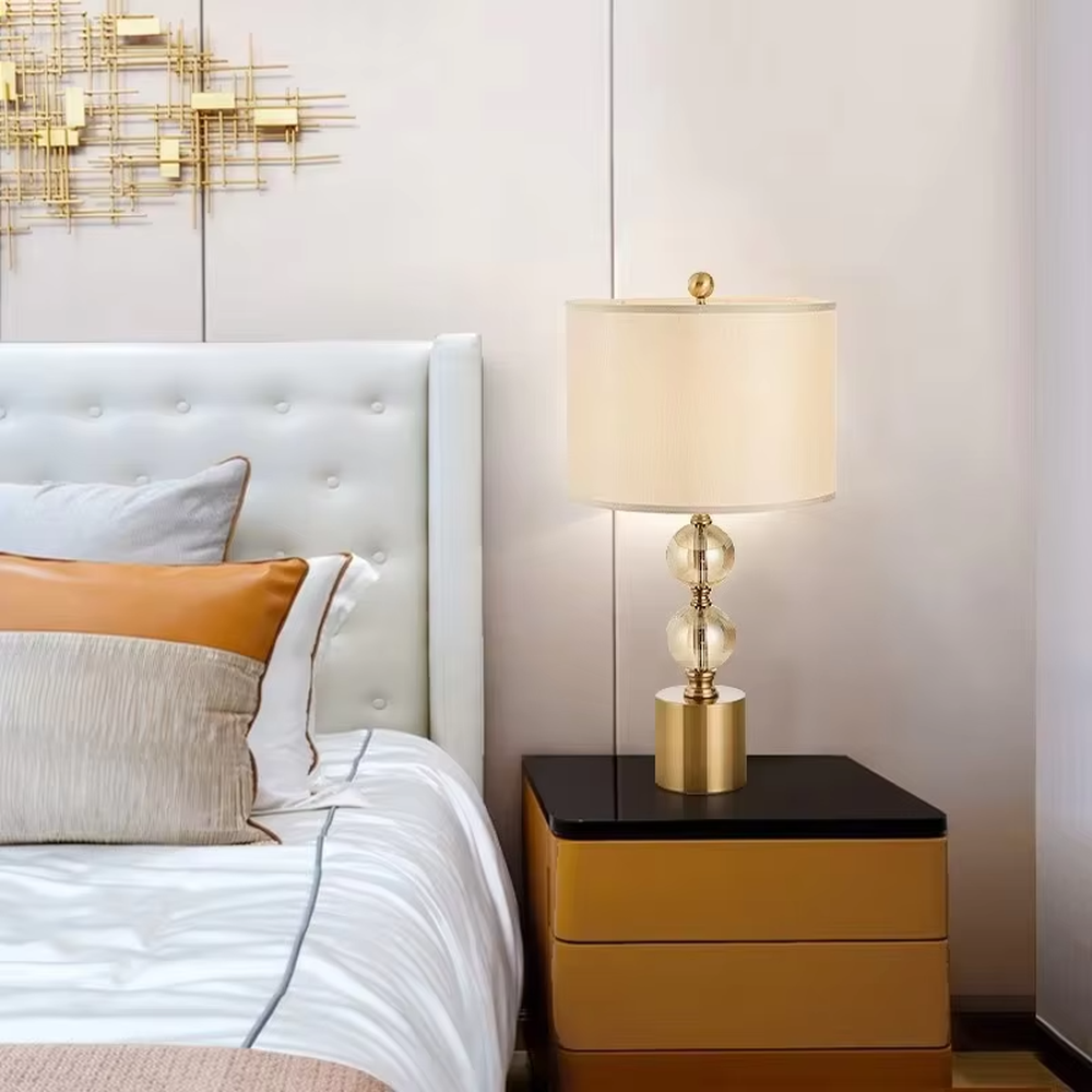 This is a luxury-style table lamp with a golden base, transparent glass spherical body, and beige fabric lampshade. It features a simple and elegant design with excellent texture. It is used for local desktop lighting and decoration, creating a luxurious and warm ambiance. It is suitable for luxury-style home bedroom bedside tables, high-end hotel guest rooms, modern apartment living spaces and other places.