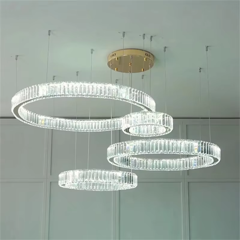 This modern light luxury multi-ring crystal chandelier consists of multiple crystal rings of varying sizes suspended in a staggered layout, each inlaid with transparent long crystals and adjustable via gold suspension wires. When lit, light refracts through the crystal to emit a brilliant and soft glow, combining layered design with an ambient atmosphere. Ideal for high-ceiling living rooms, villa foyers, hotel lobbies, or duplex spaces, it adds an exquisite and sophisticated touch to modern light luxury or minimalist environments.