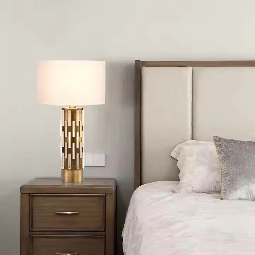 This is a modern minimalist table lamp with a golden base decorated with white vertical strips and a white fabric lampshade, featuring a simple and elegant design. It is used for local desktop lighting and decoration, combining practicality and aesthetics. It is suitable for modern home bedroom bedside tables, living room side tables, high-end hotel guest rooms, luxury apartment living spaces and other places.