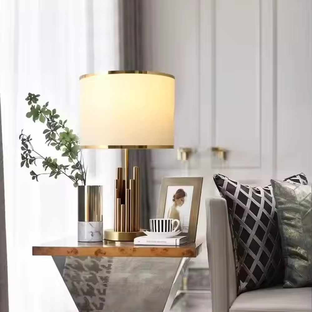 This is a modern luxury-style table lamp with a golden metal multi-column base and a beige fabric lampshade, featuring a simple and elegant design. It is used for local desktop lighting and decoration, combining practicality and aesthetics. It is suitable for modern home bedroom bedside tables, living room side tables, high-end hotel guest rooms, luxury apartment living spaces and other places.