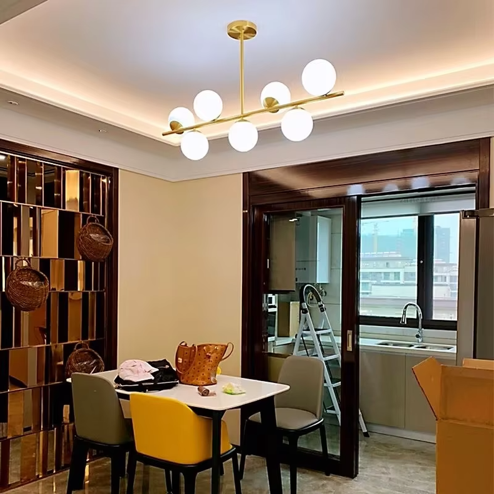 This modern minimalist linear magic bean chandelier features a gold metal frame and multiple milky white frosted glass ball lampshades, arranged in a staggered layout. When lit, it emits soft and even light, combining minimalist design with a gentle ambient atmosphere. Ideal for dining rooms, bars, kitchen islands, and other spaces, it adds an exquisite and soft touch to modern minimalist or Nordic-style home environments.