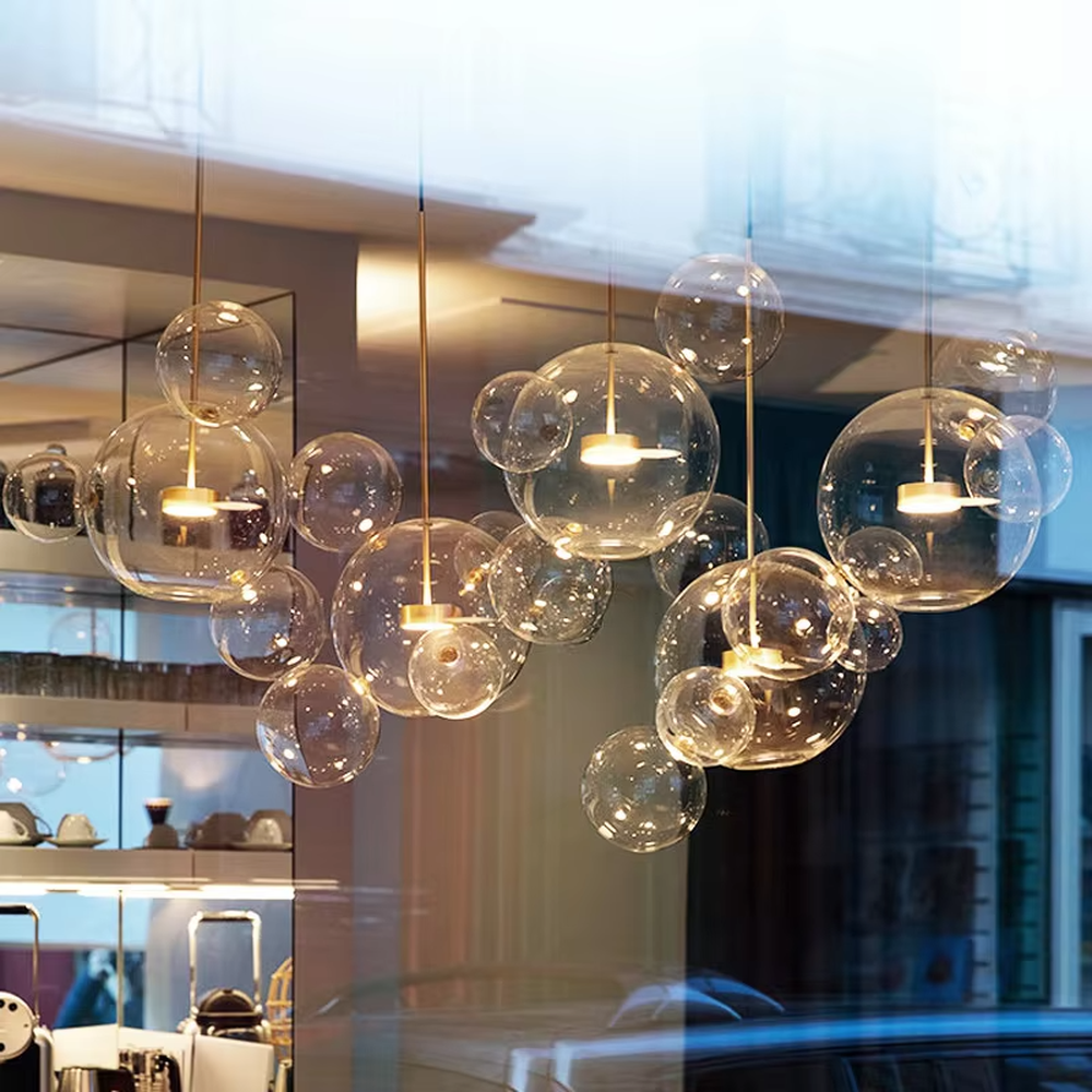 Modern art bubble cluster chandelier, featuring a cloud-like arrangement of transparent glass bubbles paired with black and gold suspension wires. Light refracts through the bubbles to create a soft and translucent glow, combining a dreamy feel and artistic ambiance, making it a high-end decorative lighting fixture that elevates the space's style.