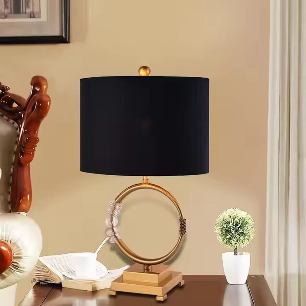 This is a luxurious retro-style table lamp with a golden circular base, a black fabric lampshade, and crystal elements, featuring an elegant and grand design. It is used for local desktop lighting and decoration, enhancing the luxurious retro ambiance of the space. It is suitable for luxury-style home living room side tables, high-end hotel guest rooms, retro-style clubs and other places.
