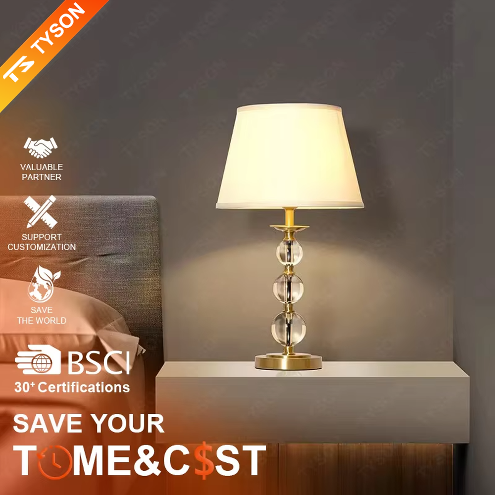 This is a luxury crystal ball table lamp with a golden metal frame, multi-layer transparent crystal balls, and a beige fabric lampshade, featuring a minimalist luxury design. It is used for local desktop lighting and decoration, creating a warm and luxurious ambiance. It is suitable for luxury-style home bedroom bedside tables, high-end hotel guest rooms, modern soft decoration display spaces and other places.