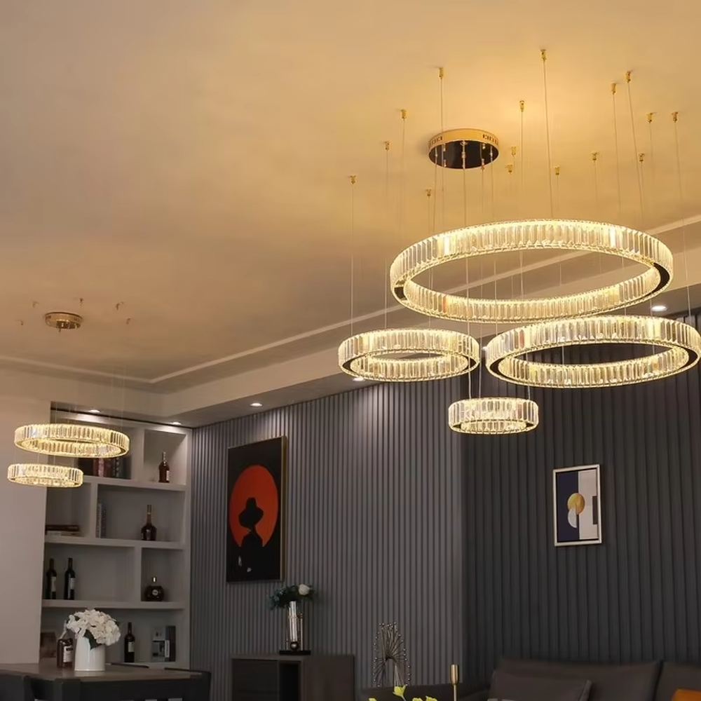 This modern light luxury multi-ring crystal chandelier consists of multiple crystal rings of varying sizes suspended in a staggered layout, each inlaid with transparent long crystals and adjustable via gold suspension wires. When lit, light refracts through the crystal to emit a brilliant and soft glow, combining layered design with an ambient atmosphere. Ideal for high-ceiling living rooms, villa foyers, hotel lobbies, or duplex spaces, it adds an exquisite and sophisticated touch to modern light luxury or minimalist environments.