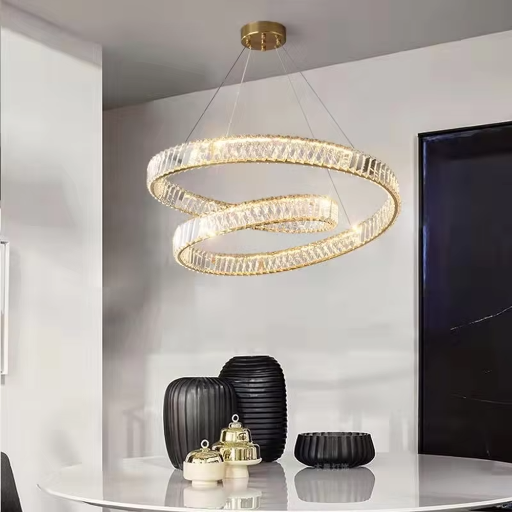This modern light luxury interwoven ring crystal chandelier features a gold metal frame, inlaid with transparent long crystals to create a dynamic interwoven double-ring shape. When lit, light refracts through the crystal to emit a brilliant and soft glow, combining a futuristic feel with an ambient atmosphere. Ideal for dining rooms, living rooms, light luxury apartments, and other spaces, it adds an exquisite and sophisticated touch to modern minimalist or light luxury home environments.