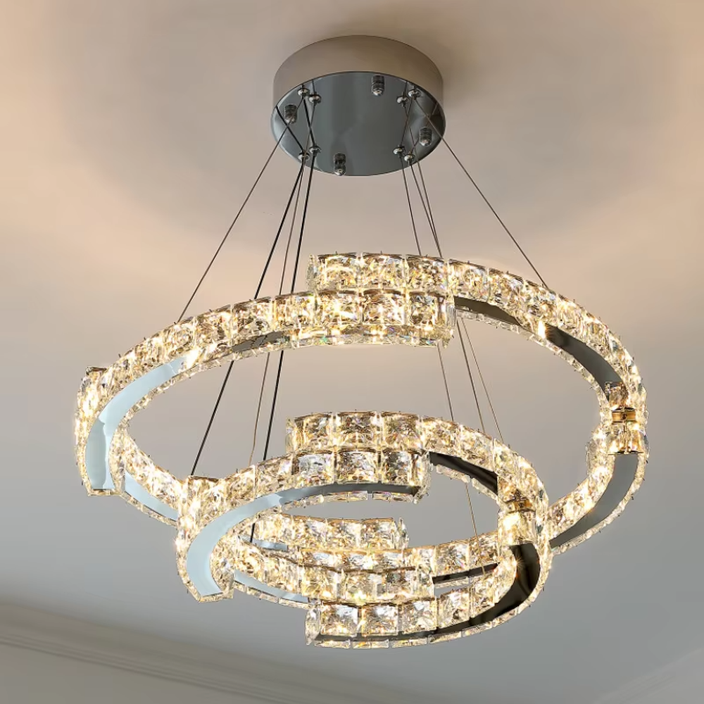 This modern light luxury double-ring interwoven crystal chandelier features a silver metal base, inlaid with transparent crystals to create a dynamic double-ring interwoven shape. When lit, light refracts through the crystal to emit a brilliant and dynamic glow, combining a futuristic feel with an ambient atmosphere. Ideal for living rooms, dining rooms, light luxury apartments, and other spaces, it adds an exquisite and sophisticated touch to modern minimalist or light luxury home environments.