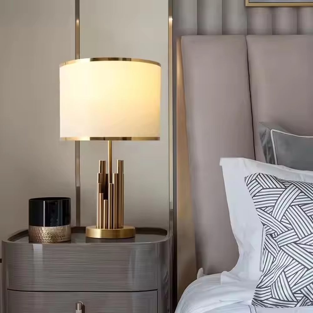 This is a modern luxury-style table lamp with a golden metal multi-column base and a beige fabric lampshade, featuring a simple and elegant design. It is used for local desktop lighting and decoration, combining practicality and aesthetics. It is suitable for modern home bedroom bedside tables, living room side tables, high-end hotel guest rooms, luxury apartment living spaces and other places.
