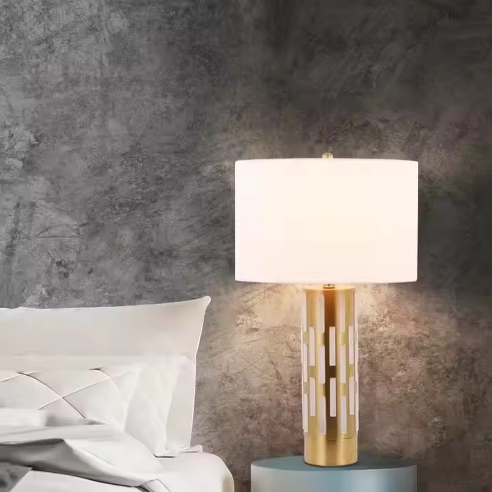 This is a modern minimalist table lamp with a golden base decorated with white vertical strips and a white fabric lampshade, featuring a simple and elegant design. It is used for local desktop lighting and decoration, combining practicality and aesthetics. It is suitable for modern home bedroom bedside tables, living room side tables, high-end hotel guest rooms, luxury apartment living spaces and other places.