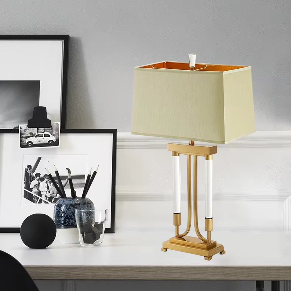 This is a retro elegant-style gold and white fabric table lamp, with a golden metal bracket (with white column elements) and a beige fabric square lampshade (orange interior). It features a retro and exquisite design, with warm and soft lighting. It is used for local desktop lighting and decoration, creating a retro and elegant atmosphere. Suitable for retro-style bedrooms, European-style living rooms, high-end homestays and other places.