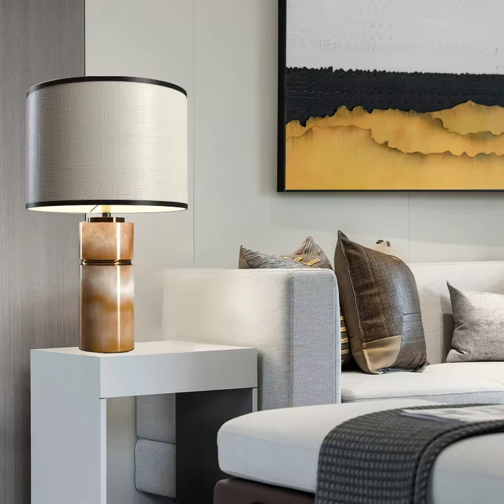 This is a light luxury minimalist table lamp, with a beige textured fabric lampshade (embellished with black trim) paired with a copper-gold layered texture base. It has an elegant and high-end style, with soft and warm lighting, creating a light luxury minimalist atmosphere.