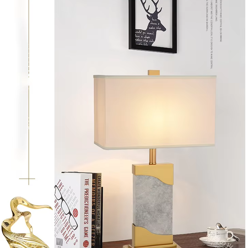 This is a luxury black-gold marble table lamp, with a golden metal frame, black-veined marble (with curved design), and a white fabric square lampshade, featuring a minimalist luxury design with high-quality texture. It is used for local desktop lighting and decoration, creating a high-end luxury atmosphere. It is suitable for luxury-style home bedroom bedside tables, high-end hotel guest rooms, modern soft decoration display spaces and other places.
