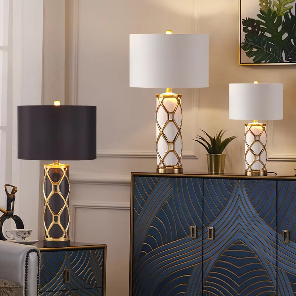 This is a luxury-style gold and white geometric hollow table lamp, with a gold geometric hollow base, white cylinder, and beige fabric circular lampshade, featuring an exquisite and elegant design with strong luxury texture. It is used for local desktop lighting and decoration, creating a luxury and warm atmosphere. Suitable for luxury-style home bedroom bedside tables, high-end hotel guest rooms, European-style living room side tables and other places.