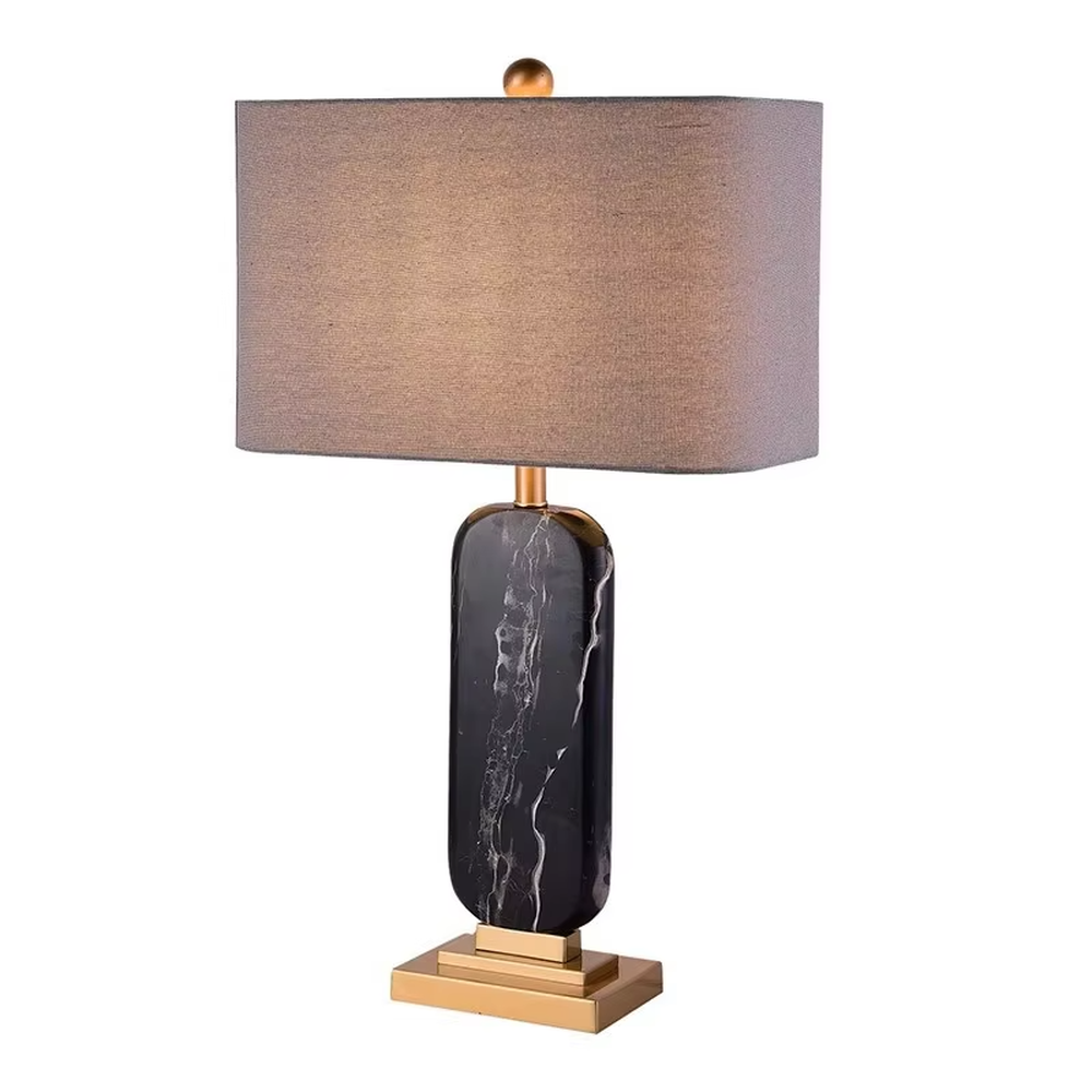 This is a luxury black-gold marble table lamp, with a black-veined marble base, golden metal components, and a gray fabric square lampshade, featuring a minimalist luxury design with high-quality texture. It is used for local desktop lighting and decoration, creating a high-end luxury atmosphere. It is suitable for luxury-style home bedroom bedside tables, high-end hotel guest rooms, modern soft decoration display spaces and other places.