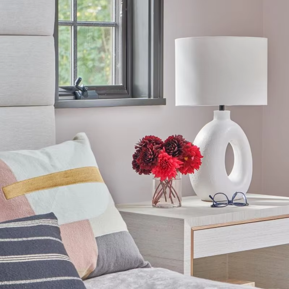 This is a modern artistic white hollow curved table lamp, with a white curved base (featuring a middle hollow design) paired with a white cylindrical lampshade. It has a minimalist artistic style and soft warm lighting.