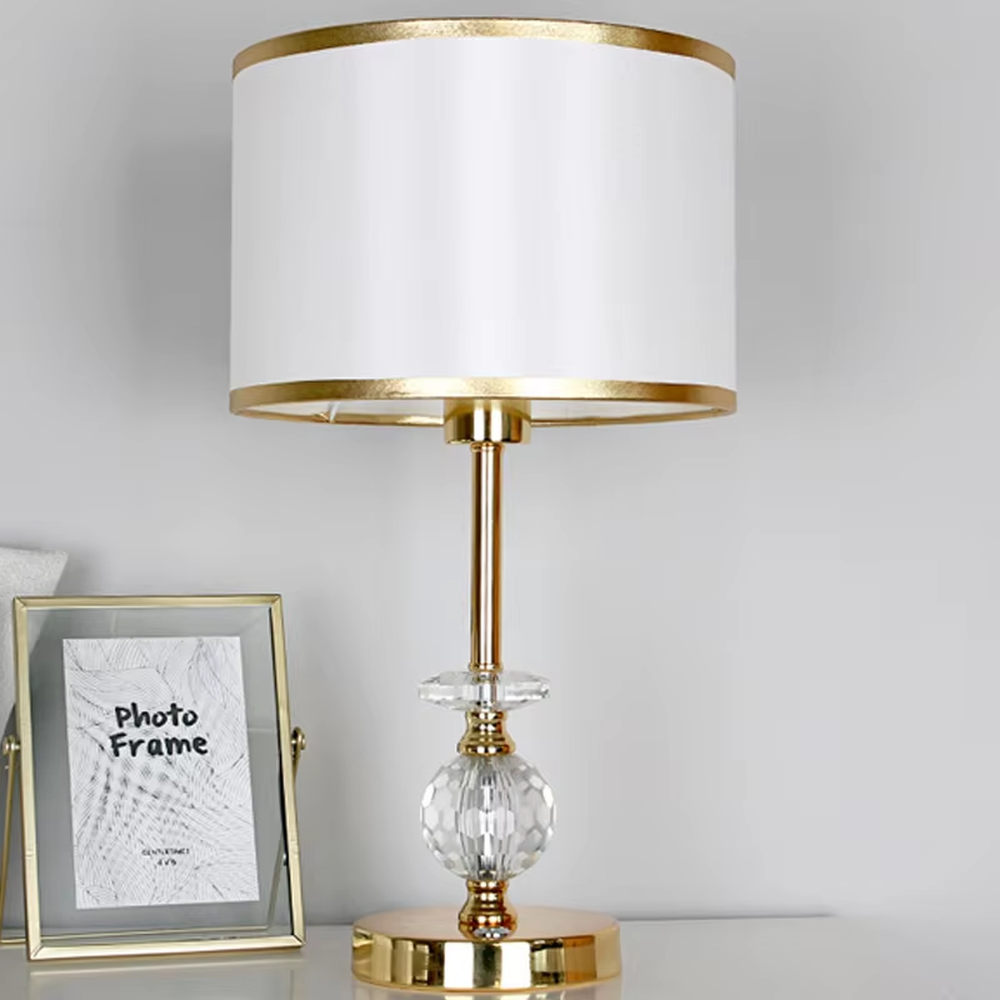 This is a light luxury exquisite fabric crystal table lamp, with a beige fabric lampshade paired with a golden trim, a golden metal lamp pole embedded with transparent cut crystal decorations, a high-quality golden base, and soft and elegant lighting, creating a light luxury exquisite atmosphere.