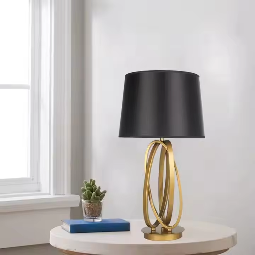 This is a modern luxury circular metal table lamp, with a golden interlaced circular metal base and a black fabric conical lampshade, featuring an artistic design and strong luxury texture. It is used for local desktop lighting and decoration, creating a high-end luxury atmosphere. It is suitable for luxury-style home bedroom bedside tables, modern minimalist living room side tables, high-end hotel guest rooms and other places.