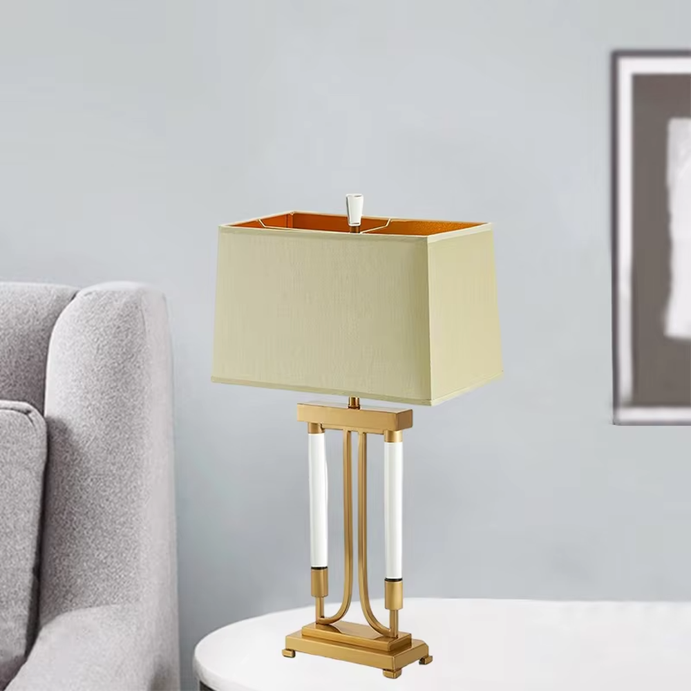 This is a retro elegant-style gold and white fabric table lamp, with a golden metal bracket (with white column elements) and a beige fabric square lampshade (orange interior). It features a retro and exquisite design, with warm and soft lighting. It is used for local desktop lighting and decoration, creating a retro and elegant atmosphere. Suitable for retro-style bedrooms, European-style living rooms, high-end homestays and other places.