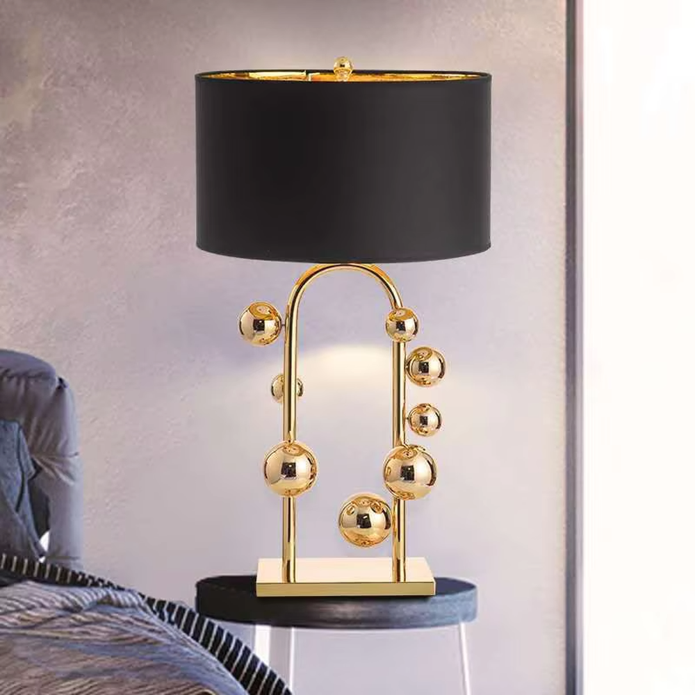 This is a light luxury modern-style golden ball table lamp, with a golden metal frame paired with multi-sized golden ball decorations, a black cylindrical lampshade + a golden square base, featuring a high-end and exquisite style, with soft and stylish lighting.