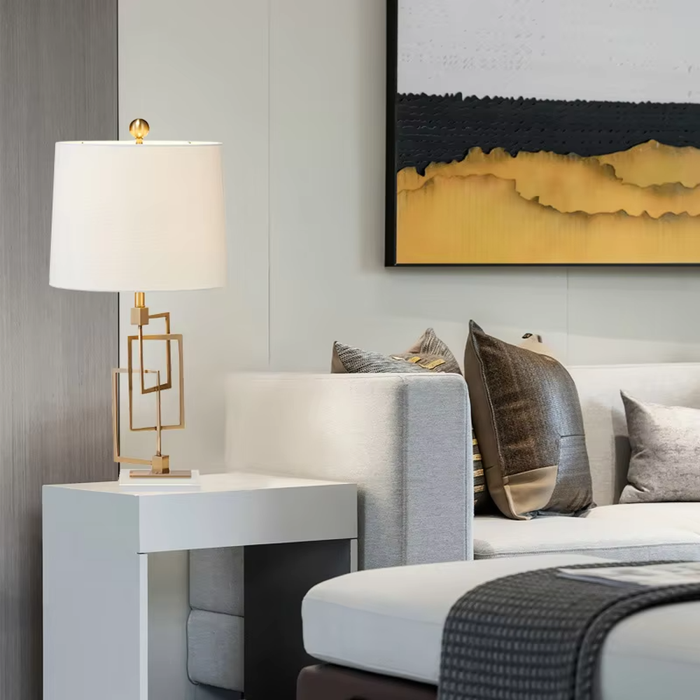 Light luxury modern geometric square frame gold stand table lamp, golden multi-layer square frame stand + beige fabric cylindrical lampshade + white stone base, soft and high-end lighting, creating a light luxury minimalist atmosphere.