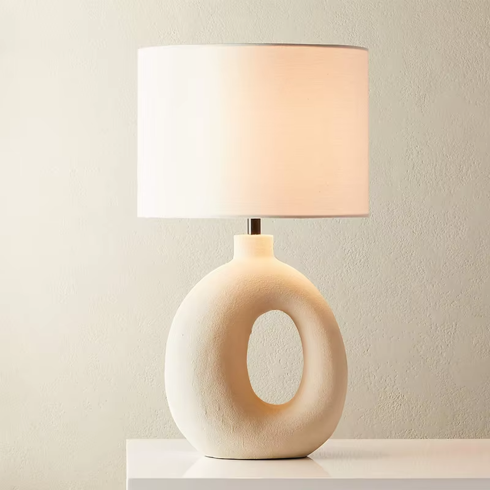 This is a modern artistic white hollow curved table lamp, with a white curved base (featuring a middle hollow design) paired with a white cylindrical lampshade. It has a minimalist artistic style and soft warm lighting.