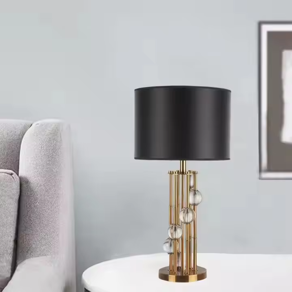 This is a luxury black-gold crystal table lamp, with a golden metal column (with multiple thin columns design) and transparent crystal balls, a black cylindrical fabric lampshade, featuring a modern luxury design with high-quality texture. It is used for local desktop lighting and decoration, creating a high-end luxury atmosphere. It is suitable for luxury-style home bedroom bedside tables, high-end hotel guest rooms, modern soft decoration display spaces and other places.