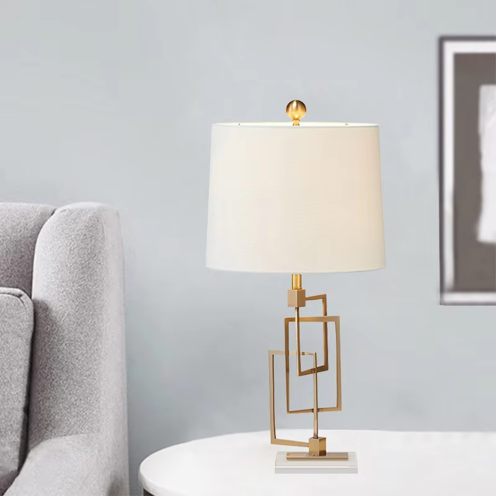 Light luxury modern geometric square frame gold stand table lamp, golden multi-layer square frame stand + beige fabric cylindrical lampshade + white stone base, soft and high-end lighting, creating a light luxury minimalist atmosphere.
