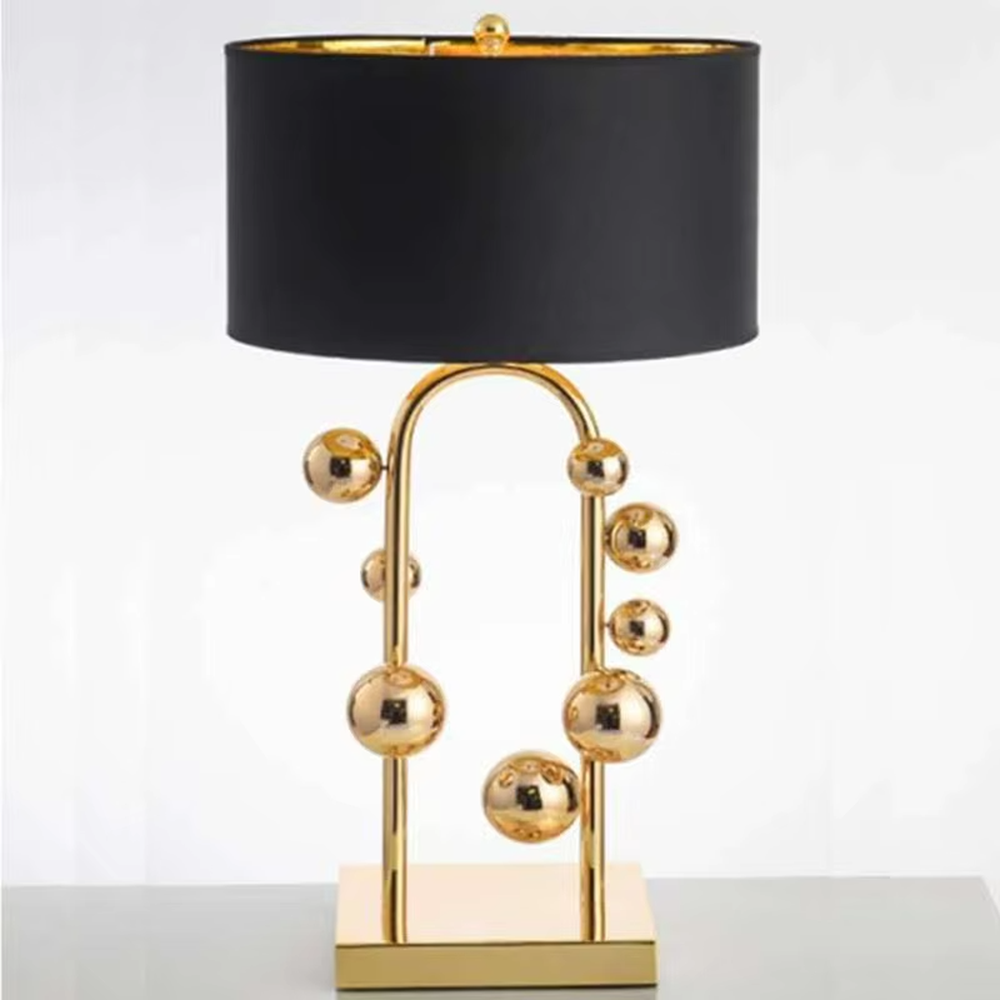 This is a light luxury modern-style golden ball table lamp, with a golden metal frame paired with multi-sized golden ball decorations, a black cylindrical lampshade + a golden square base, featuring a high-end and exquisite style, with soft and stylish lighting.