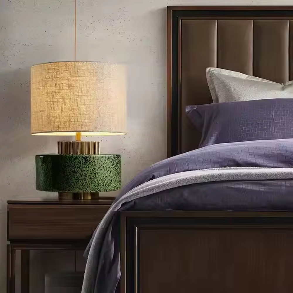 This is a modern artistic green and gold table lamp, with a green textured base, golden metal ring, and beige fabric circular lampshade, featuring a minimalist and grand design with both artistic sense and texture. It is used for local desktop lighting and decoration, creating a modern artistic atmosphere. It is suitable for modern minimalist home bedroom bedside tables, artistic-style living room side tables, high-end hotel guest rooms and other places.