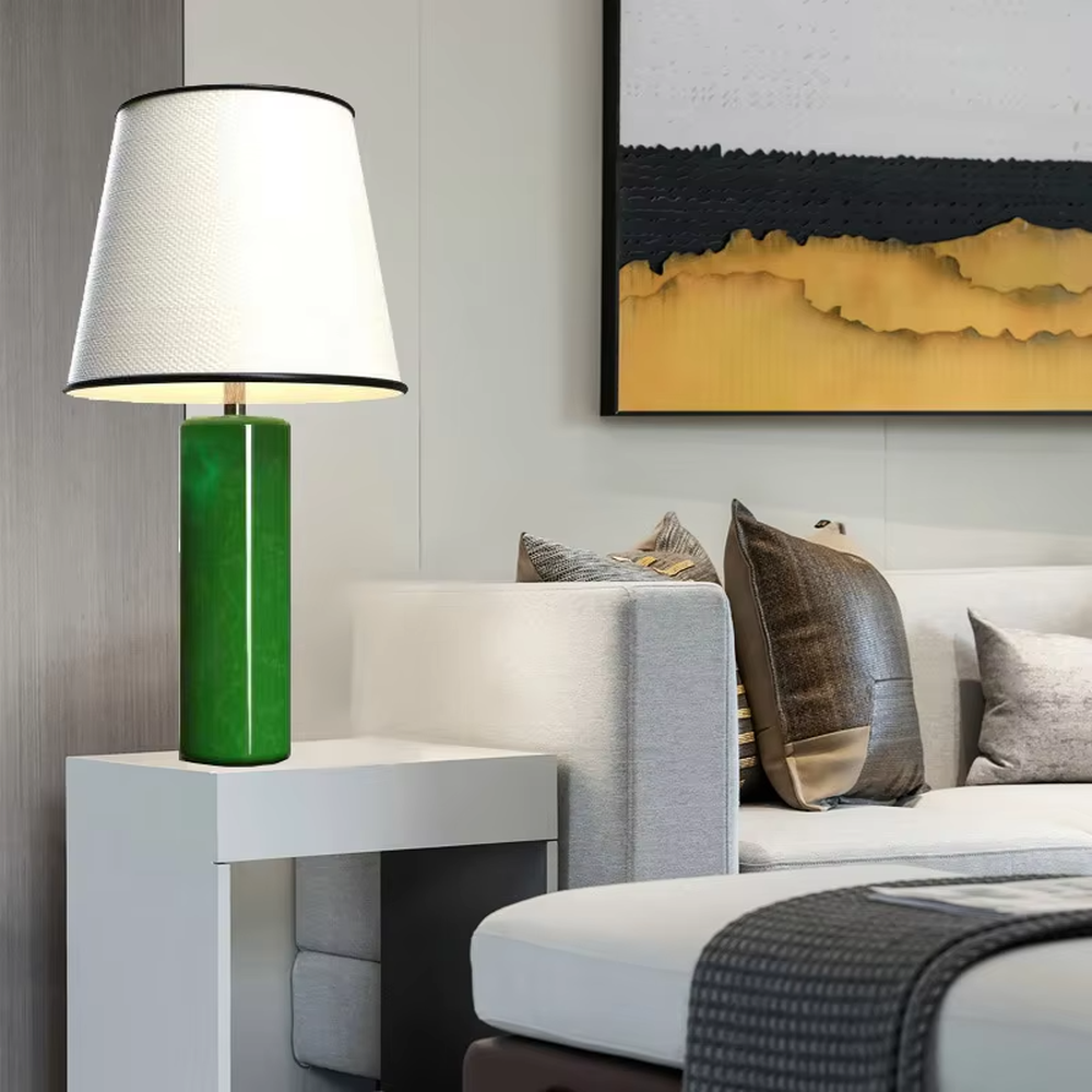 This is a modern fresh-style green cylindrical table lamp, with a green cylindrical base and a white fabric lampshade (black edging), featuring a minimalist modern design and fresh style. It is used for local desktop lighting and decoration, creating a fresh and modern atmosphere. Suitable for modern minimalist bedroom bedside tables, Nordic-style living room side tables, creative studios and other places.