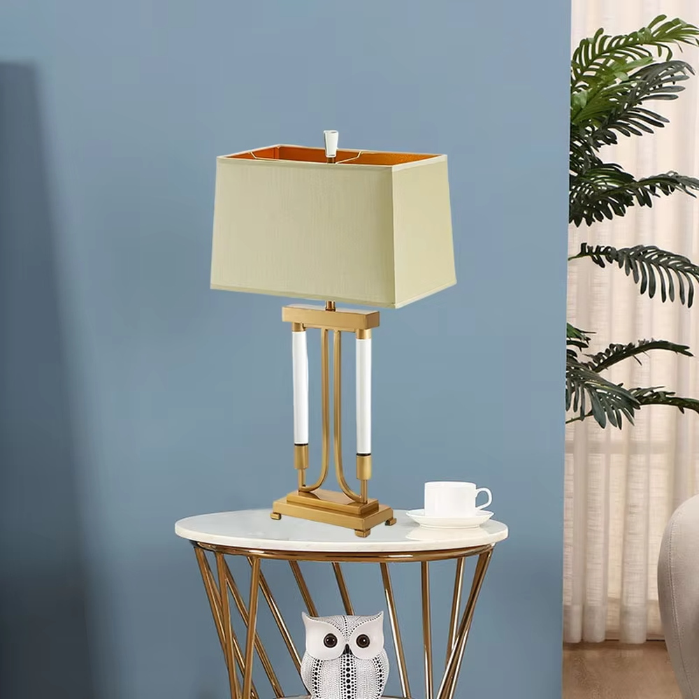 This is a retro elegant-style gold and white fabric table lamp, with a golden metal bracket (with white column elements) and a beige fabric square lampshade (orange interior). It features a retro and exquisite design, with warm and soft lighting. It is used for local desktop lighting and decoration, creating a retro and elegant atmosphere. Suitable for retro-style bedrooms, European-style living rooms, high-end homestays and other places.