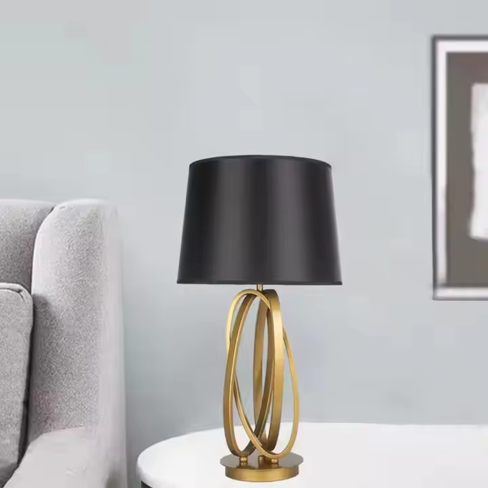 This is a modern luxury circular metal table lamp, with a golden interlaced circular metal base and a black fabric conical lampshade, featuring an artistic design and strong luxury texture. It is used for local desktop lighting and decoration, creating a high-end luxury atmosphere. It is suitable for luxury-style home bedroom bedside tables, modern minimalist living room side tables, high-end hotel guest rooms and other places.