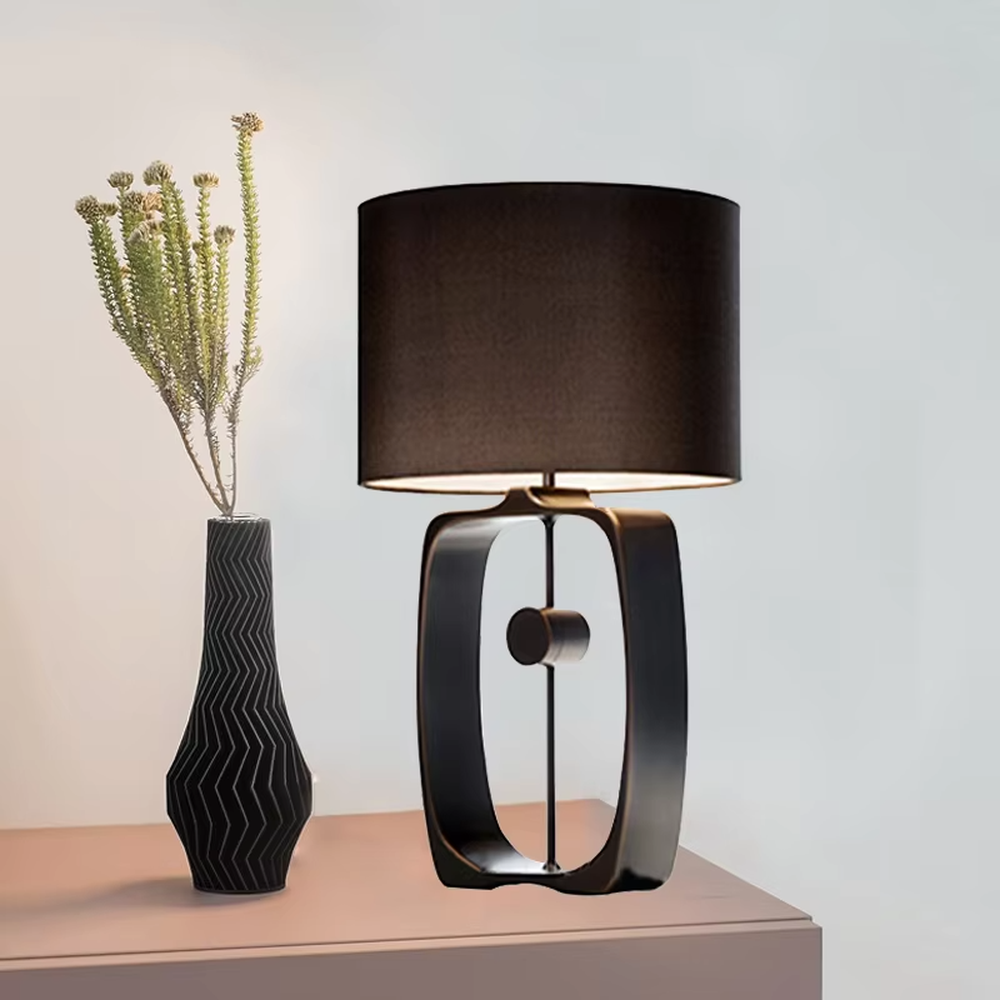 Modern minimalist black hollow frame table lamp, black fabric cylindrical lampshade + metal hollow rectangular base, soft and high-end lighting, creating a minimalist textured atmosphere.