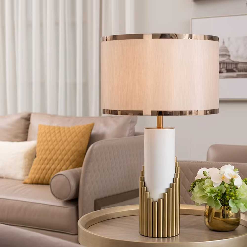 This is a light luxury-style gold and white metal fabric table lamp, with a golden staggered metal column base, paired with a white cylinder and a beige fabric lampshade (golden edging). It features a minimalist light luxury design, with warm and soft lighting. It is used for local desktop lighting and decoration, creating a light luxury and warm atmosphere. Suitable for light luxury-style bedroom bedside tables, modern minimalist living room side tables, high-end hotel guest rooms and other places.