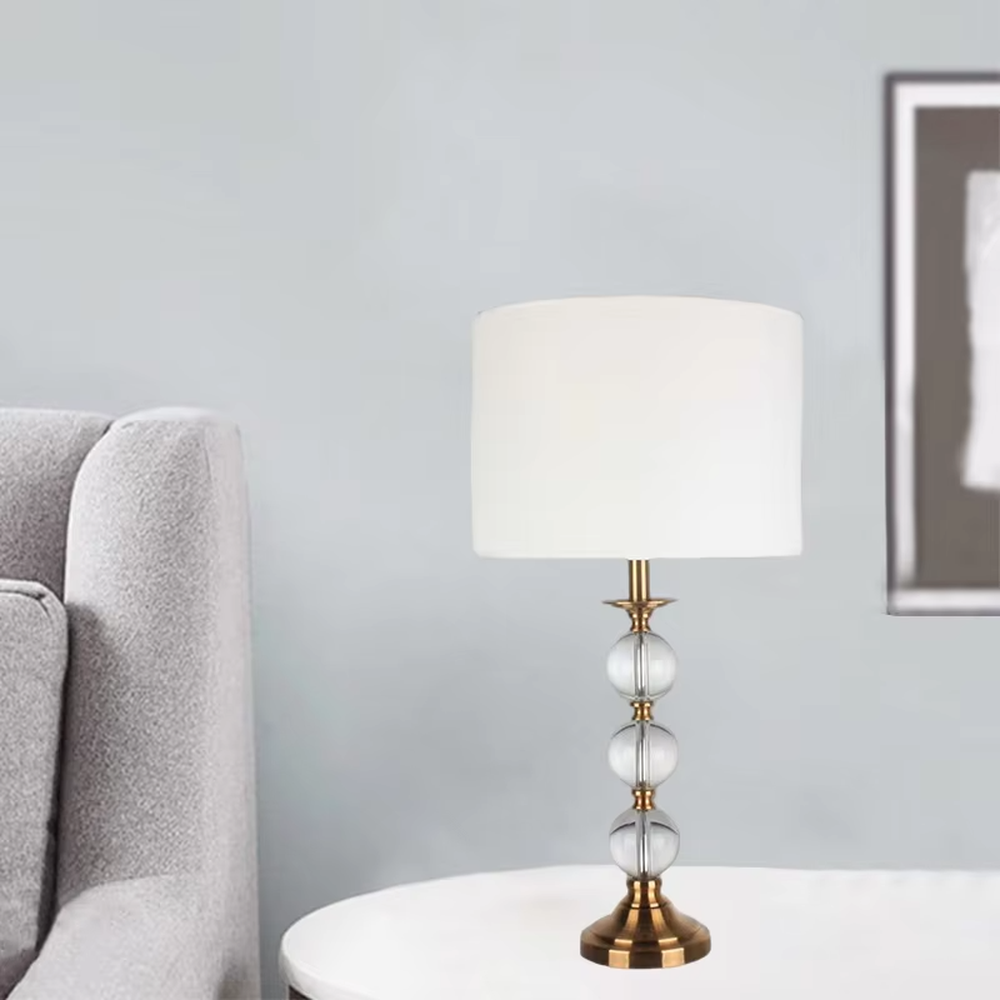 This is a light luxury exquisite crystal ball column table lamp, with a golden metal base and connectors, paired with transparent crystal balls and a white fabric round lampshade. It features a light luxury and exquisite design, with warm and soft lighting. It is used for local desktop lighting and decoration, creating a light luxury elegant atmosphere. Suitable for light luxury-style bedroom bedside tables, modern minimalist living room side tables, high-end hotel guest rooms and other places.