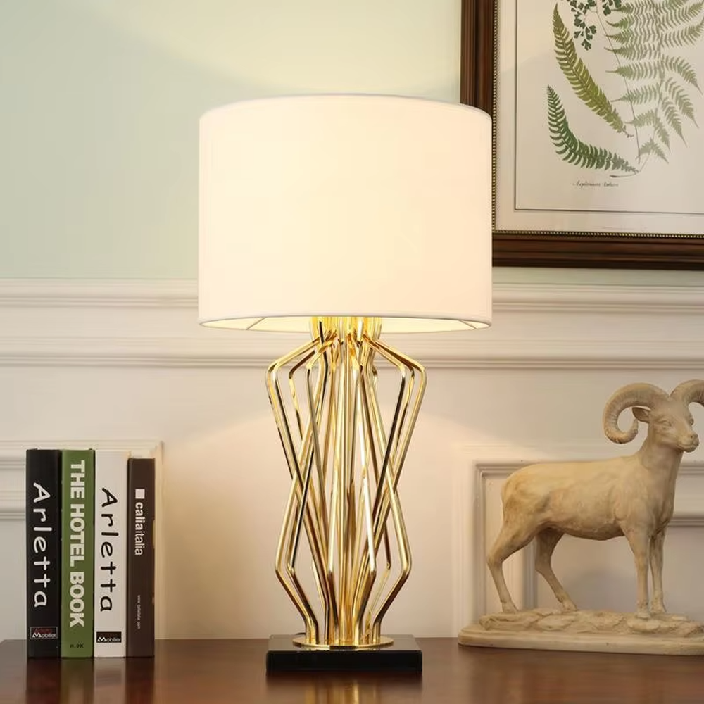 Light luxury golden interlaced hollow table lamp, white cylindrical fabric lampshade + black base, soft and warm lighting, creating a high-end elegant atmosphere.