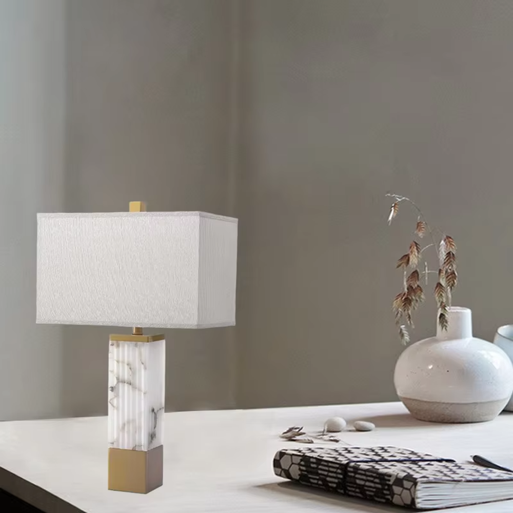 This is a luxury marble table lamp, with a white marble (textured) base, golden metal components, and a white fabric square lampshade, featuring a minimalist luxury design with high-quality texture. It is used for local desktop lighting and decoration, creating a high-end luxury atmosphere. It is suitable for luxury-style home bedroom bedside tables, high-end hotel guest rooms, modern soft decoration display spaces and other places.
