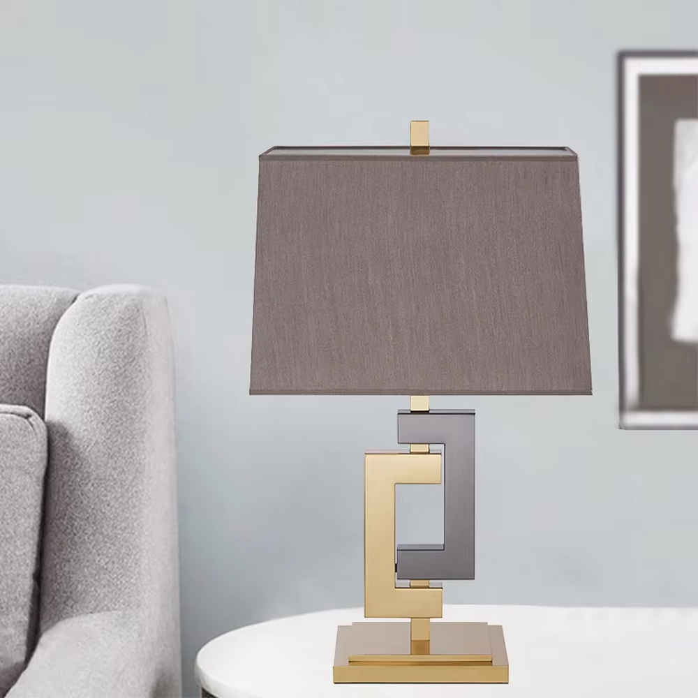 Light luxury gold-gray color-blocking geometric square frame table lamp, gold + dark gray metal geometric stand + dark gray fabric rectangular lampshade, soft and high-end lighting, creating a light luxury modern atmosphere.