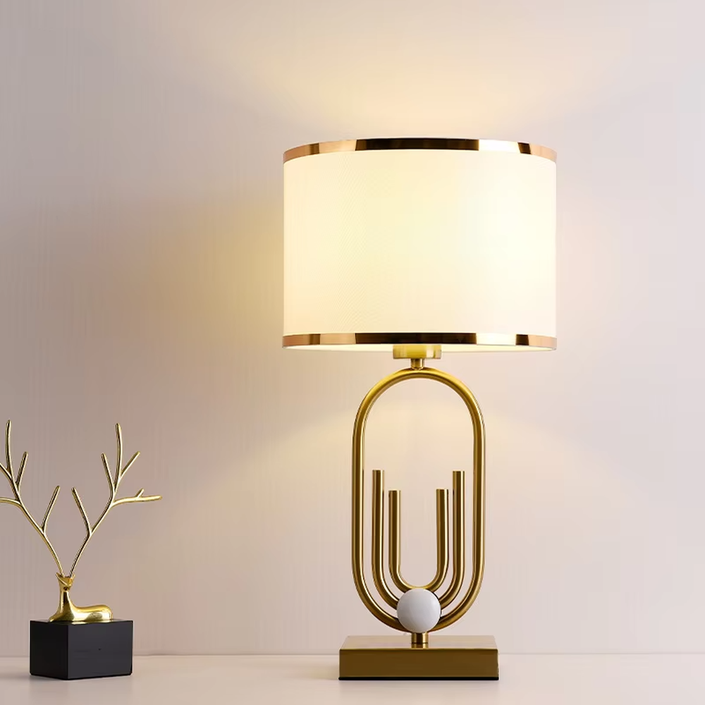 Light luxury golden geometric line base table lamp, beige fabric gold-edged lampshade + golden U-shaped multi-layer frame + white small ball decoration, soft warm light, creating a modern light luxury atmosphere.