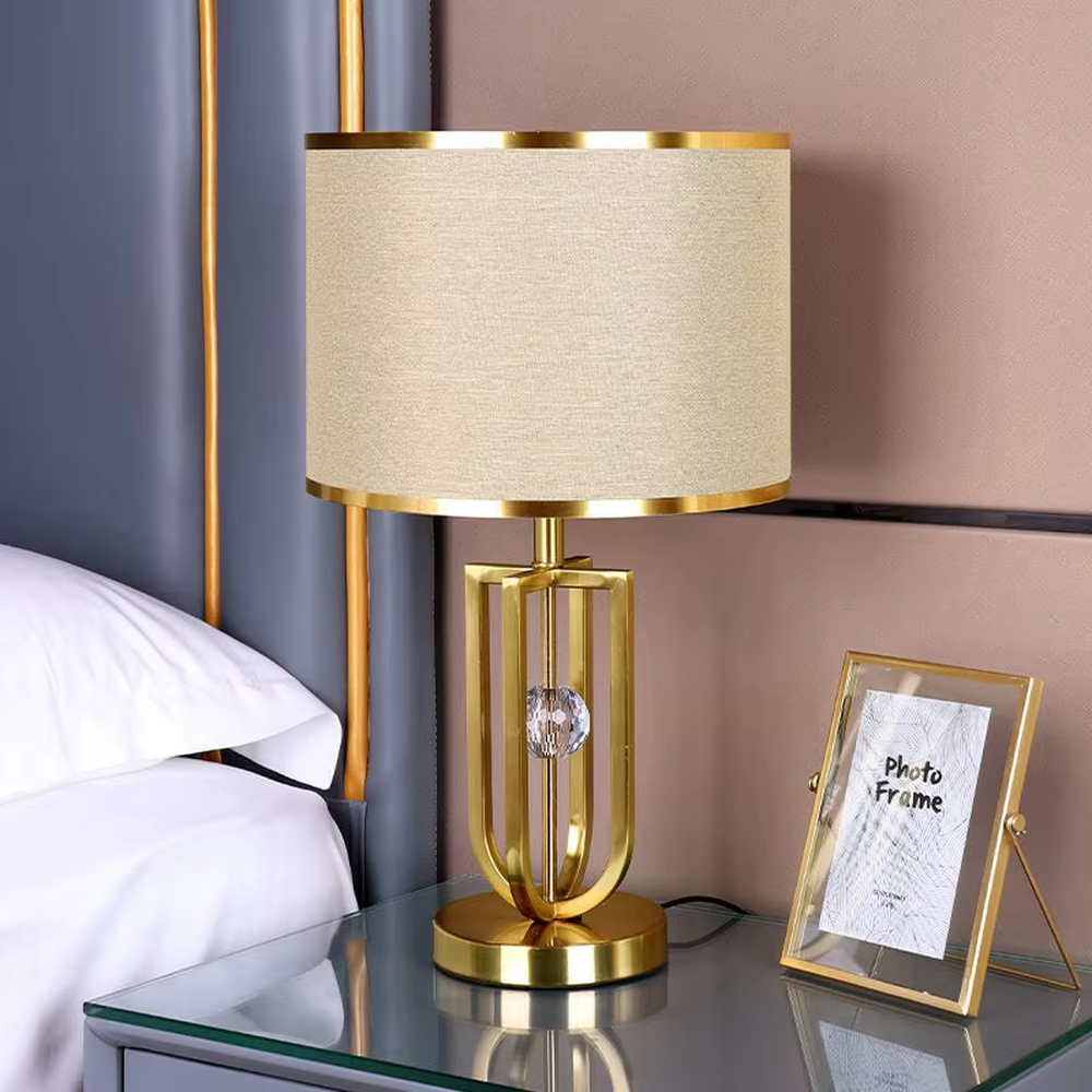 Light luxury golden geometric line base table lamp, beige fabric gold-edged lampshade + golden U-shaped multi-layer frame + white small ball decoration, soft warm light, creating a modern light luxury atmosphere.