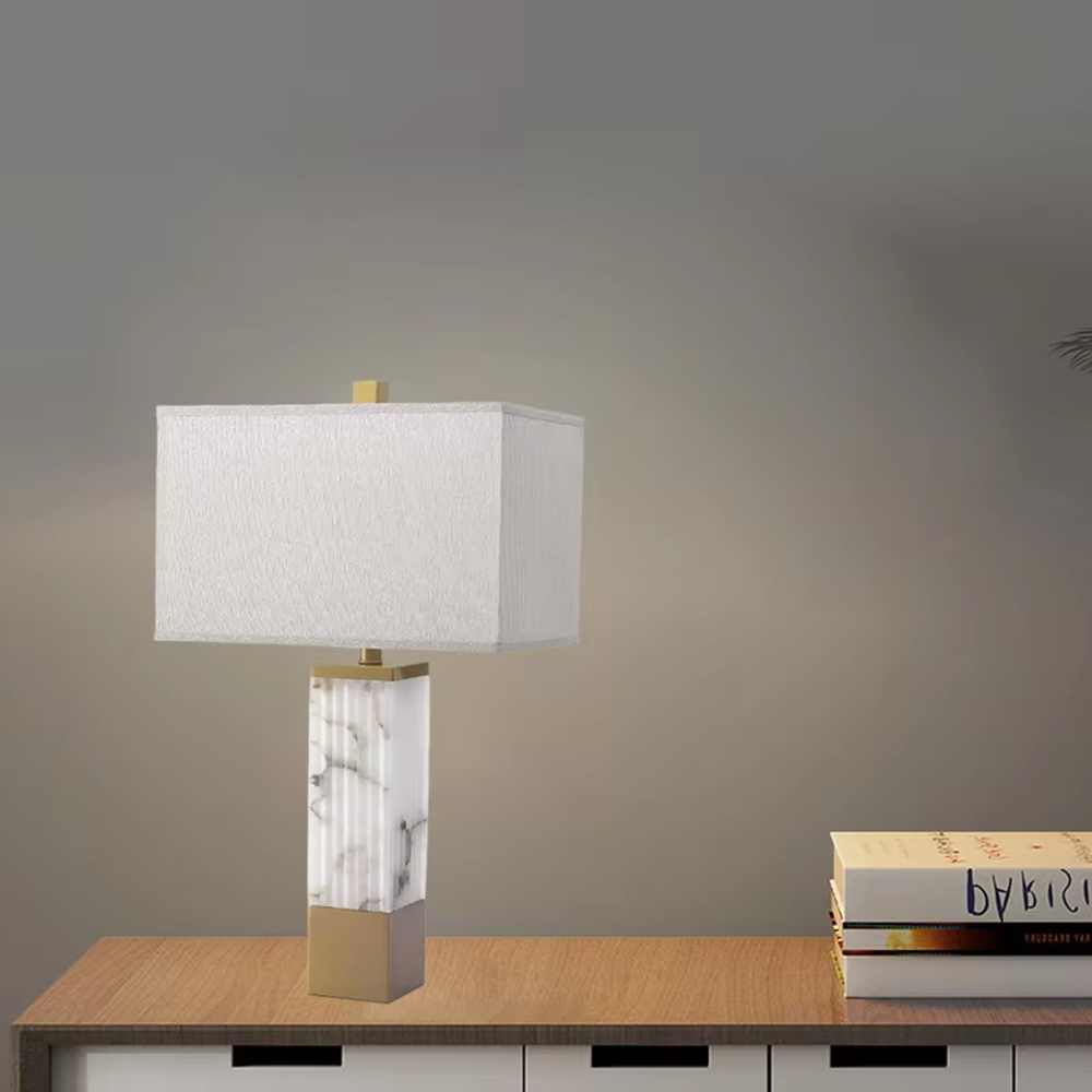 This is a luxury marble table lamp, with a white marble (textured) base, golden metal components, and a white fabric square lampshade, featuring a minimalist luxury design with high-quality texture. It is used for local desktop lighting and decoration, creating a high-end luxury atmosphere. It is suitable for luxury-style home bedroom bedside tables, high-end hotel guest rooms, modern soft decoration display spaces and other places.