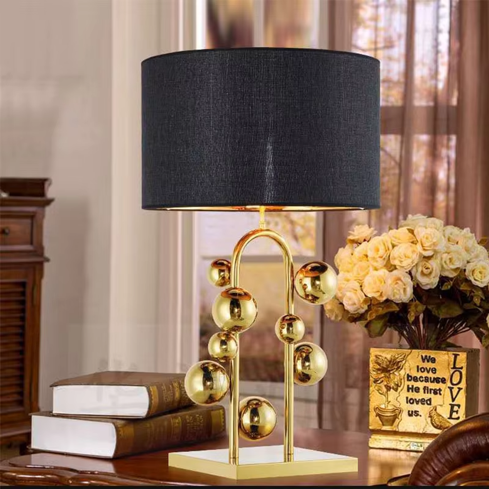 This is a light luxury modern-style golden ball table lamp, with a golden metal frame paired with multi-sized golden ball decorations, a black cylindrical lampshade + a golden square base, featuring a high-end and exquisite style, with soft and stylish lighting.