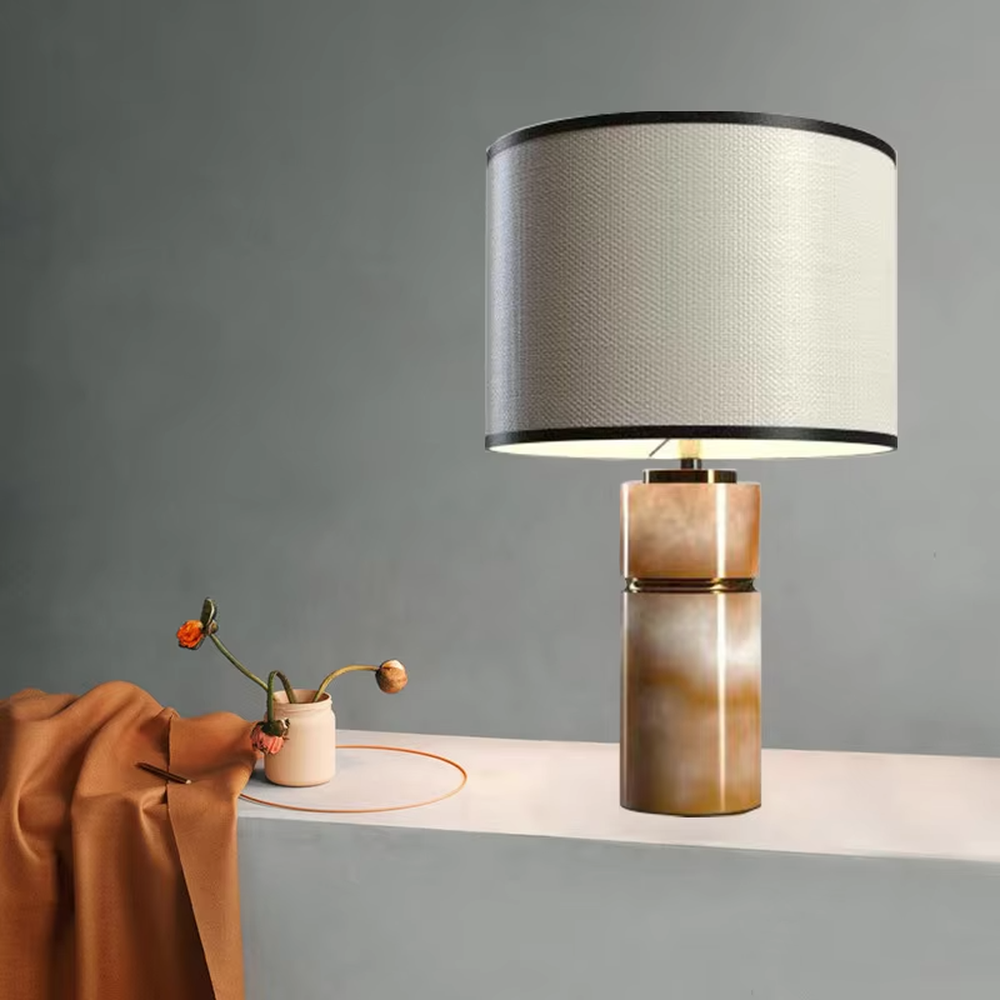 This is a light luxury minimalist table lamp, with a beige textured fabric lampshade (embellished with black trim) paired with a copper-gold layered texture base. It has an elegant and high-end style, with soft and warm lighting, creating a light luxury minimalist atmosphere.