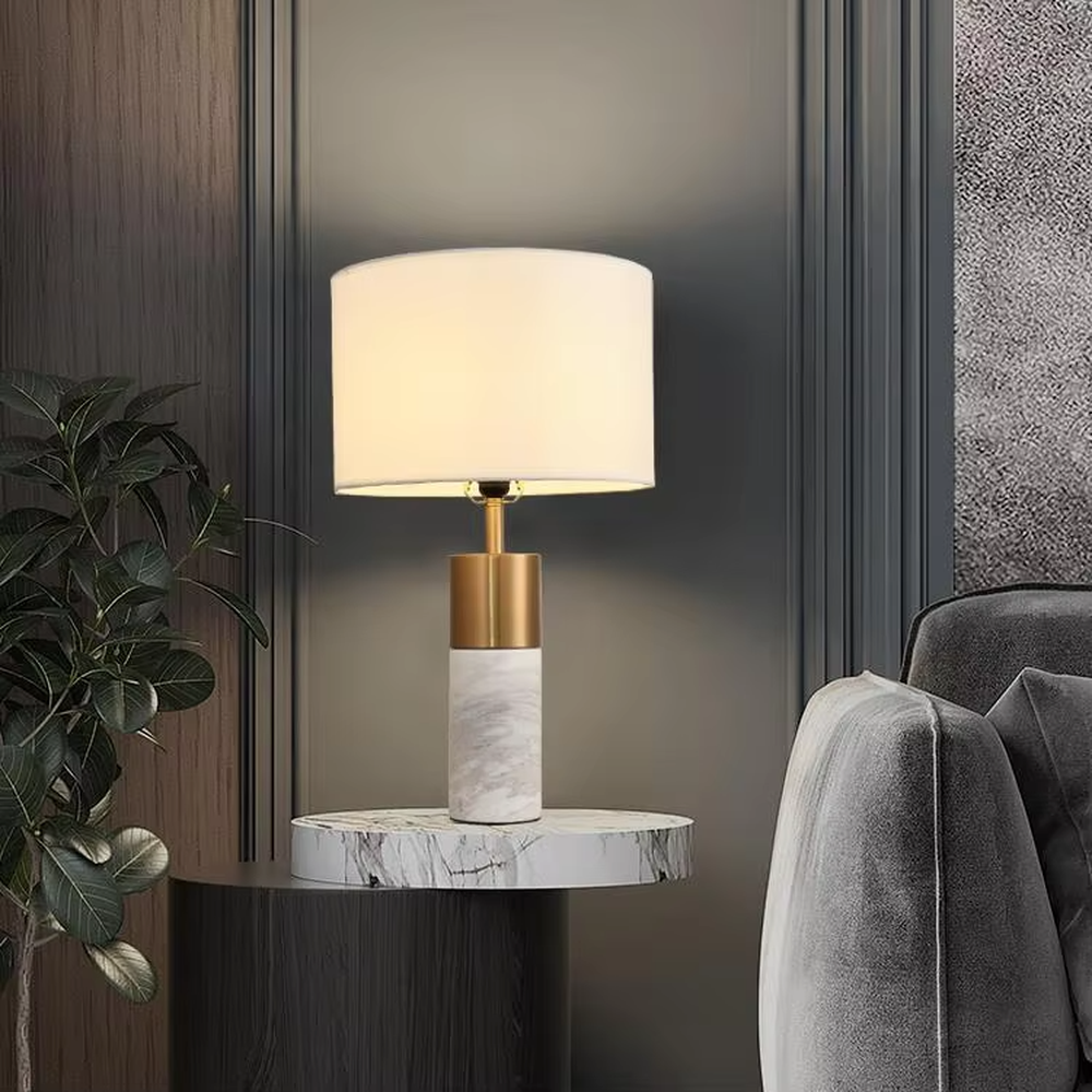 Light luxury gold-decor white marble cylindrical base table lamp, beige fabric cylindrical lampshade, soft warm light, creating a simple high-end light luxury atmosphere.