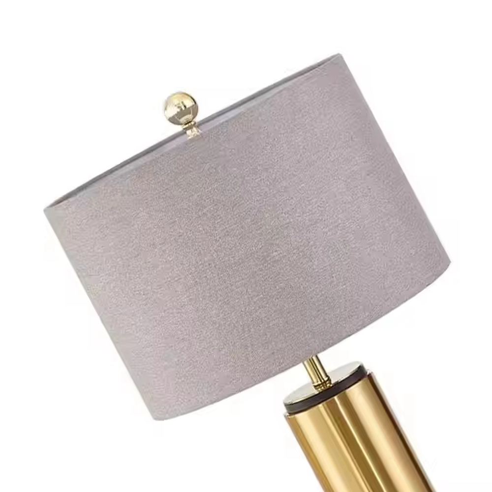 This is a light luxury minimalist golden cylinder table lamp, with a golden metal cylinder base paired with a light purple textured fabric lampshade, decorated with a small golden ball on top. The lighting is soft and warm, creating an elegant light luxury atmosphere.