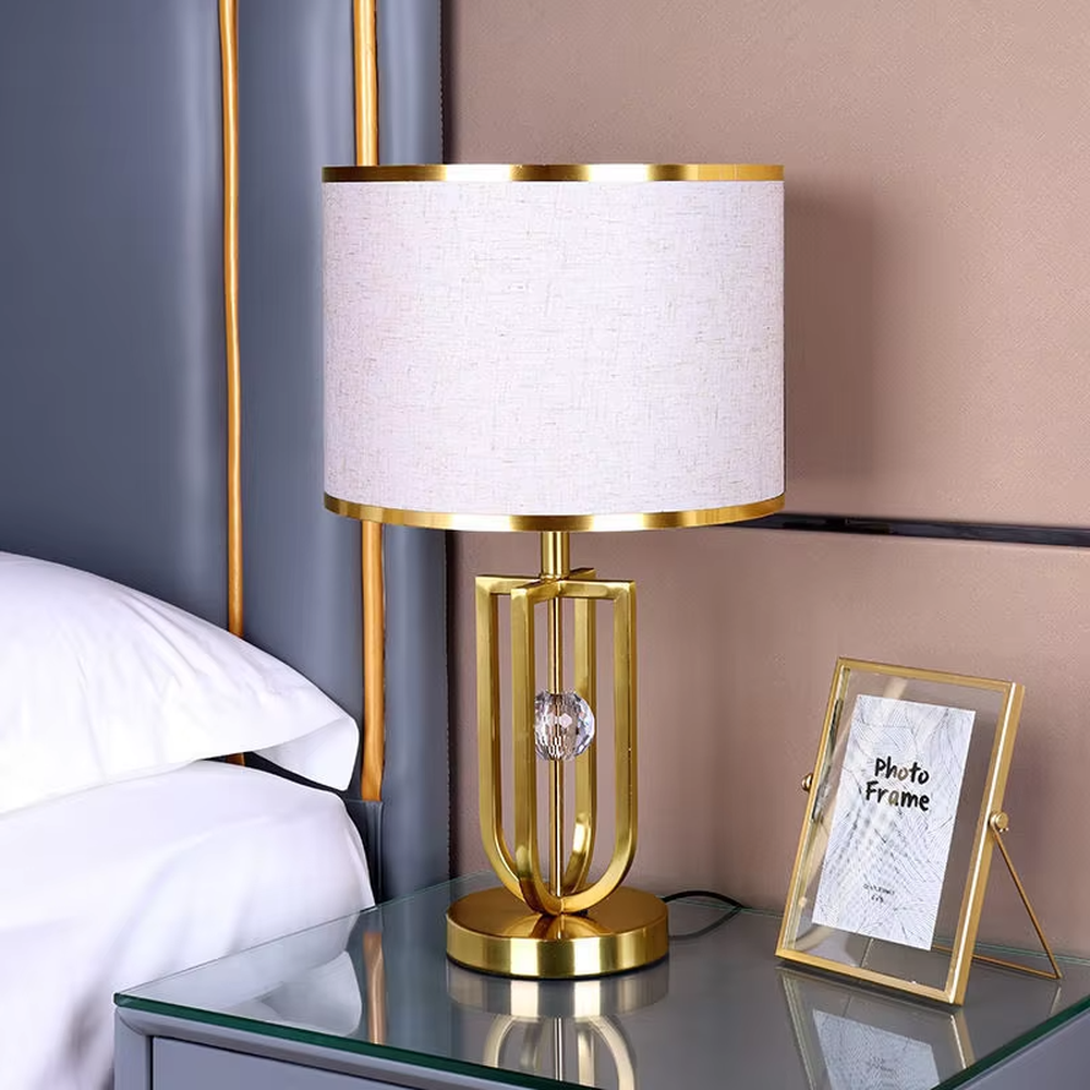 This is a light luxury artistic golden oval metal table lamp, with a golden metal oval frame with line decorations, paired with a beige fabric round lampshade. It features a light luxury and elegant design, with warm and soft lighting. It is used for local desktop lighting and decoration, creating a light luxury artistic atmosphere. Suitable for light luxury-style bedroom bedside tables, modern minimalist living room side tables, high-end hotel guest rooms and other places.